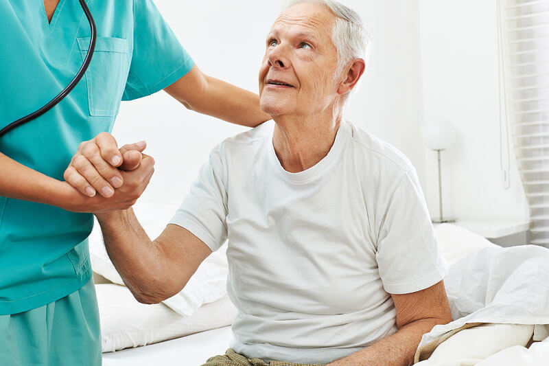 Caregiver helping older man get up from bed