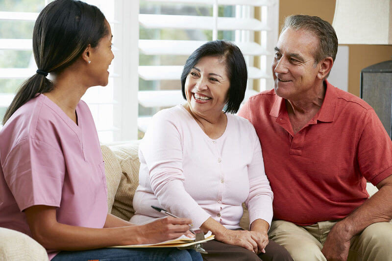 Nurse making notes during home visit with senior couple