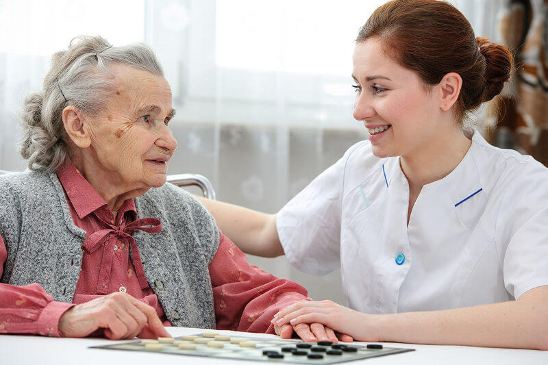 Senior woman playing checkers with a nurse in a retirement home