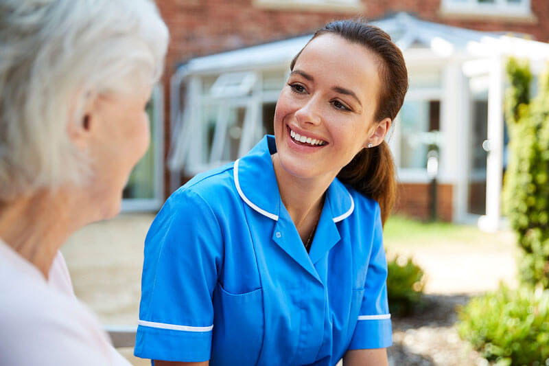 Senior woman sitting on bench and talking with nurse in retirement home